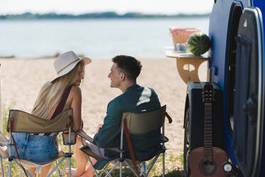 Ein junges Paar sitzt in den Sommerferien zusammen vor einem Van und unterhält sich. - HPIF12565