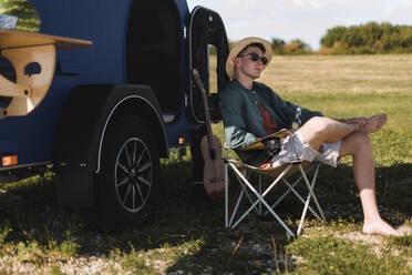 Ein junger Mann sitzt vor einem Lieferwagen und genießt den Sommer. - HPIF12570