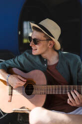 Junger Mann sitzt im Van und spielt auf der Gitarre, genießt den Sommer. - HPIF12571