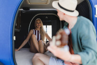 Ein glückliches junges Paar sitzt zusammen in einem Van, zeltet und spielt auf einem Gitarrenstuhl. - HPIF12572