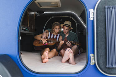 Ein glückliches junges Paar sitzt zusammen in einem Van, zeltet und spielt auf einem Gitarrenstuhl. - HPIF12574