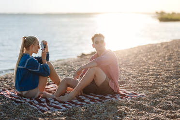 Junges Mädchen fotografiert ihren Freund am Strand bei Sonnenuntergang. - HPIF12587