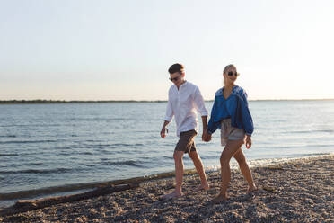 Happy young couple walking on a beach during sunset, prepairing for a picnic. - HPIF12591