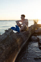 Young man sitting on tree stump in lake during sunset. - HPIF12596