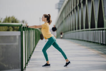 Junge Frau beim Dehnen in einer Stadt, Vorbereitung auf einen Lauf, gesunder Lebensstil und Sportkonzept. - HPIF12617