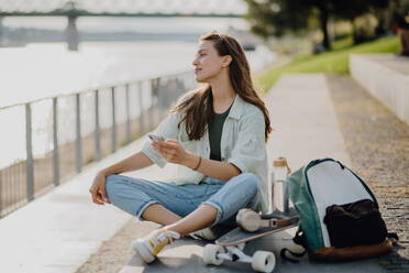 Happy young woman sitting in city park and scrolling smartphone. Youth culture and commuting concept. - HPIF12629
