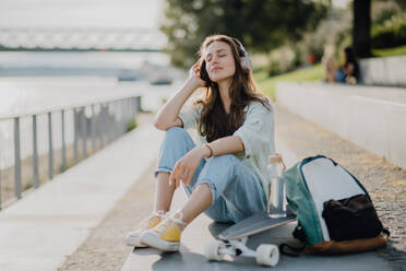 Happy young woman sitting in a city and listening music. Youth culture and commuting concept. - HPIF12630