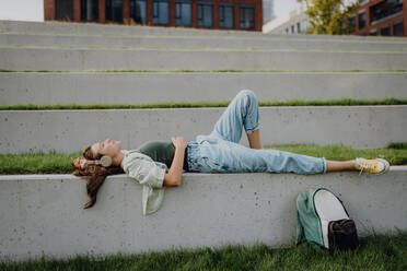 Junge Frau ruht sich im Stadtpark mit geschlossenen Augen aus und genießt die Musik über Kopfhörer. - HPIF12633