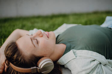 Portrait of young woman lying on a lawn listening the music trough headphones. - HPIF12634