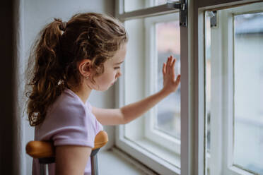 Kleines Mädchen mit gebrochenem Bein schaut aus dem Fenster. - HPIF12685