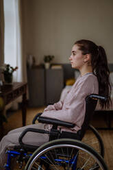 Unglückliches Teenager-Mädchen, das im Rollstuhl sitzt und aus dem Fenster schaut. - HPIF12701