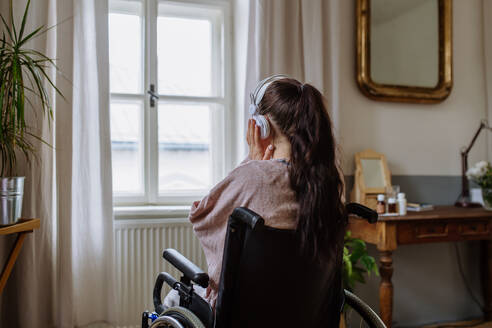 Teenager-Mädchen sitzt im Rollstuhl, hört Musik und schaut aus dem Fenster. - HPIF12703