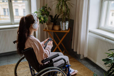 Unglückliches Teenager-Mädchen, das im Rollstuhl sitzt und aus dem Fenster schaut. - HPIF12704