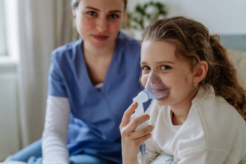 Kleines Mädchen mit Inhalator im Krankenhauszimmer, eine Krankenschwester kümmert sich um sie. - HPIF12713