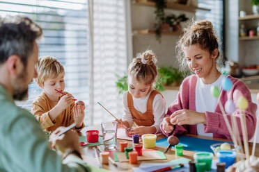 Glückliche Familie mit kleinen Kindern beim Verzieren von Ostereiern in ihrem Haus. - HPIF12732