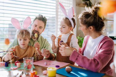 Glückliche Familie mit kleinen Kindern beim Verzieren von Ostereiern in ihrem Haus. - HPIF12734