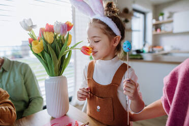 Kleines Mädchen riecht an einem Strauß Tulpenblüten, während sie mit ihrer Familie Ostereier dekoriert. - HPIF12738