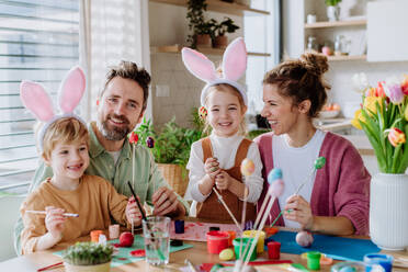 Glückliche Familie mit kleinen Kindern beim Verzieren von Ostereiern in ihrem Haus. - HPIF12740