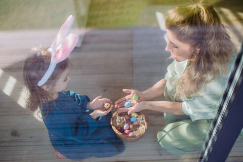 Ein kleines Mädchen hält einen Korb und zeigt der Mutter die Ostereier, die sie gefunden hat. - HPIF12801