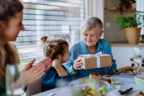 Großmutter, die ihrer Enkelin während eines Osteressens ein Geschenk überreicht. - HPIF12840