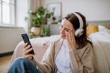 Junge Frau hört Musik über Kopfhörer in der Wohnung. - HPIF12855