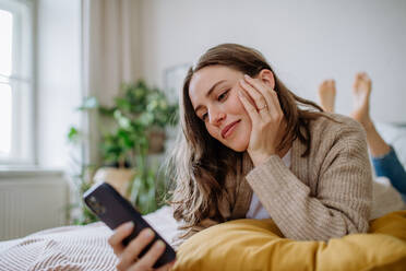 Junge Frau scrollt auf ihrem Smartphone in einer Wohnung. - HPIF12857