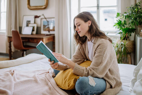 Junge Frau genießt ihre Freizeit in ihrer Wohnung und liest ein Buch. - HPIF12862