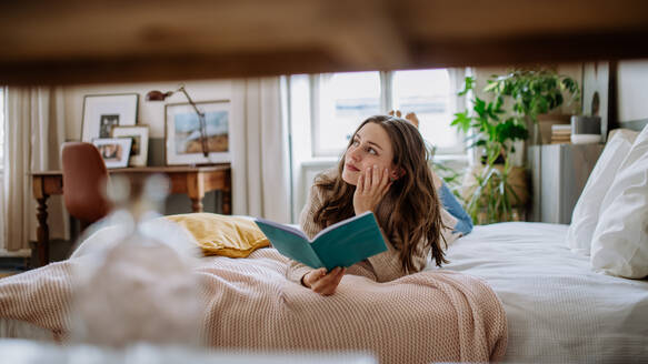 Junge Frau genießt ihre Freizeit in ihrer Wohnung und liest ein Buch. - HPIF12863