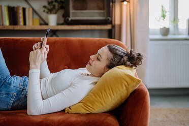 Junge Frau scrollt auf ihrem Smartphone in einer Wohnung. - HPIF12874