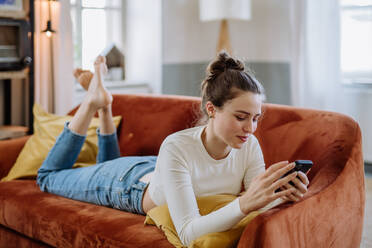 Junge Frau scrollt auf ihrem Smartphone in einer Wohnung. - HPIF12876