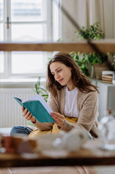 Junge Frau genießt ihre Freizeit in ihrer Wohnung und liest ein Buch. - HPIF12904