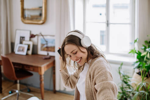 Junge Frau hört Musik über Kopfhörer in der Wohnung. - HPIF12906