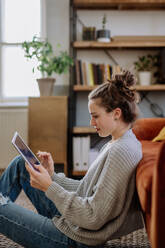 Junge Frau mit digitalem Tablet, die sich in der Wohnung ausruht. - HPIF12917