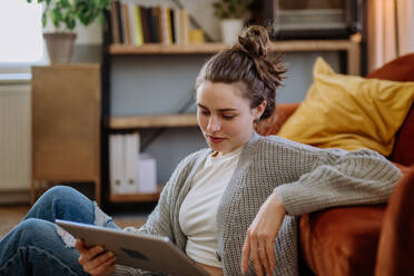 Junge Frau mit digitalem Tablet, die sich in der Wohnung ausruht. - HPIF12918