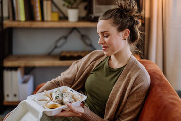 Junge Frau genießt das gelieferte Essen im Wohnzimmer. - HPIF12919