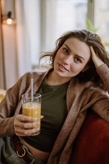 Junge Frau sitzt mit einem Getränk auf dem Sofa. - HPIF12933