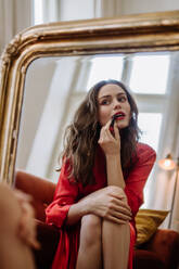 Young woman in elegant dress preparing for an evening, finishing her make up. - HPIF12939