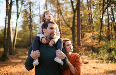 Beautiful young family with small daughter on a walk in autumn forest, having fun. - HPIF12964