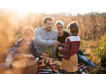 Schöne junge Familie mit kleinen Kindern beim Picknick in der herbstlichen Natur, sitzend im Gras. - HPIF12972