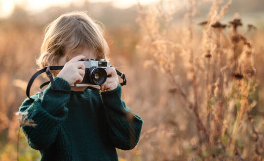 Kleines Mädchen in der herbstlichen Natur, das mit der Kamera fotografiert, Kopierraum. - HPIF12980