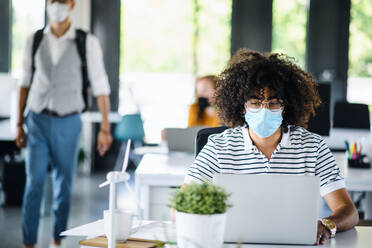 Porträt eines jungen Mannes mit Gesichtsmaske, der nach der Abriegelung wieder in seinem Büro arbeitet. - HPIF12985