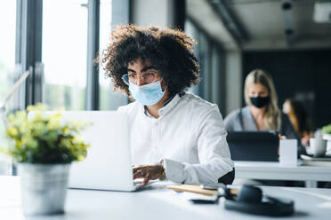 Portrait of young man with face mask back at work in office after lockdown, working. - HPIF12988