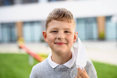 Porträt eines glücklichen Jungen mit Gesichtsmaske, der nach der Schließung des Covid-19 in die Schule zurückkehrt und in die Kamera schaut. - HPIF12991
