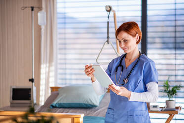 Ein Porträt einer Ärztin oder Krankenschwester, die in einem Krankenhauszimmer steht und ein Tablet benutzt. - HPIF12998