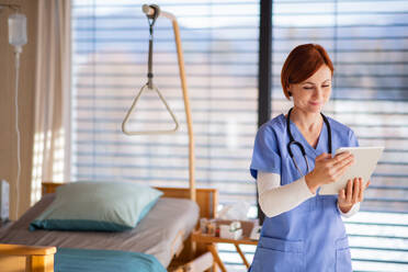 Ein Porträt einer Ärztin oder Krankenschwester, die in einem Krankenhauszimmer steht und ein Tablet benutzt. - HPIF12999