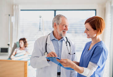 Porträt eines männlichen Oberarztes, der in einem Krankenhauszimmer steht und mit einer Krankenschwester spricht. - HPIF13005