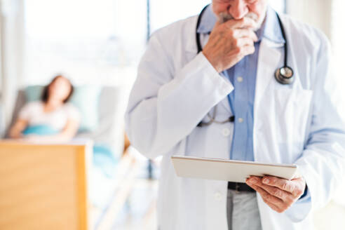 Ein nicht erkennbarer älterer männlicher Arzt steht in einem Krankenhauszimmer und benutzt ein Tablet. - HPIF13010