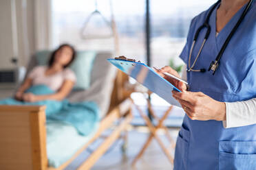 Ein nicht erkennbarer Arzt oder eine Krankenschwester steht in einem Krankenhauszimmer und hält ein Klemmbrett. - HPIF13013