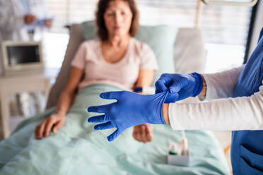 An unrecognizable doctor with patient in bed in hospital, putting on gloves. - HPIF13023