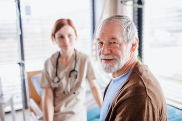 Ein älterer männlicher Patient und ein Arzt sitzen auf einem Bett im Krankenhaus und schauen in die Kamera. - HPIF13036